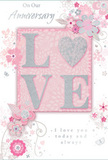 This image shows an anniversary card whose design balances romantic detail with soft, understated elegance, the kind often chosen by couples celebrating in and around Isleworth. At its centre, the word LOVE is displayed in prominent, slightly raised letters, each one outlined with a fine border of silvery glitter. The glitter lends a delicate sparkle, subtle and refined, much like the glint of a vase on a windowsill overlooking the Thames. The letters are set on a block of blush pink that deepens the tone just enough to stand out against the card's overall soft pink background. Around this focal point, a graceful spray of stylised flowers, slender leaves, and looping vines unfurls. The blooms are illustrated rather than photographic, sketched with thin, flowing lines in shades of blush, white, and cool grey, with light touches of silver highlighting certain petals and flourishes. This detailing suggests the artistry of a florist mapping out stems and blossoms for an anniversary bouquet destined for a home near Syon Lane or along Twickenham Road. The floral motifs appear to drift and swirl, creating a sense of quiet movement and gentle celebration. Tucked thoughtfully within the design is an elegant script message, expressing heartfelt anniversary wishes and enduring love in a distinctive, looping hand. The card as a whole feels like a paper echo of a soft, romantic garden scene, perfectly paired with an anniversary arrangement delivered by a local Isleworth florist to mark another year of shared memories and tender moments.